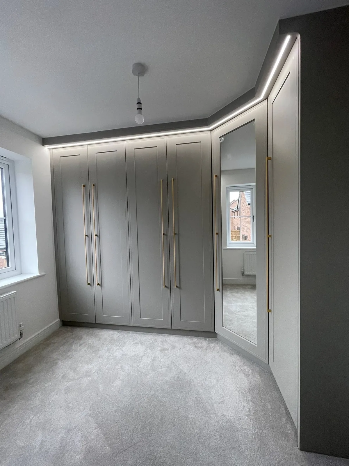 Grey fitted wardrobes beside a window with integrated lighting
