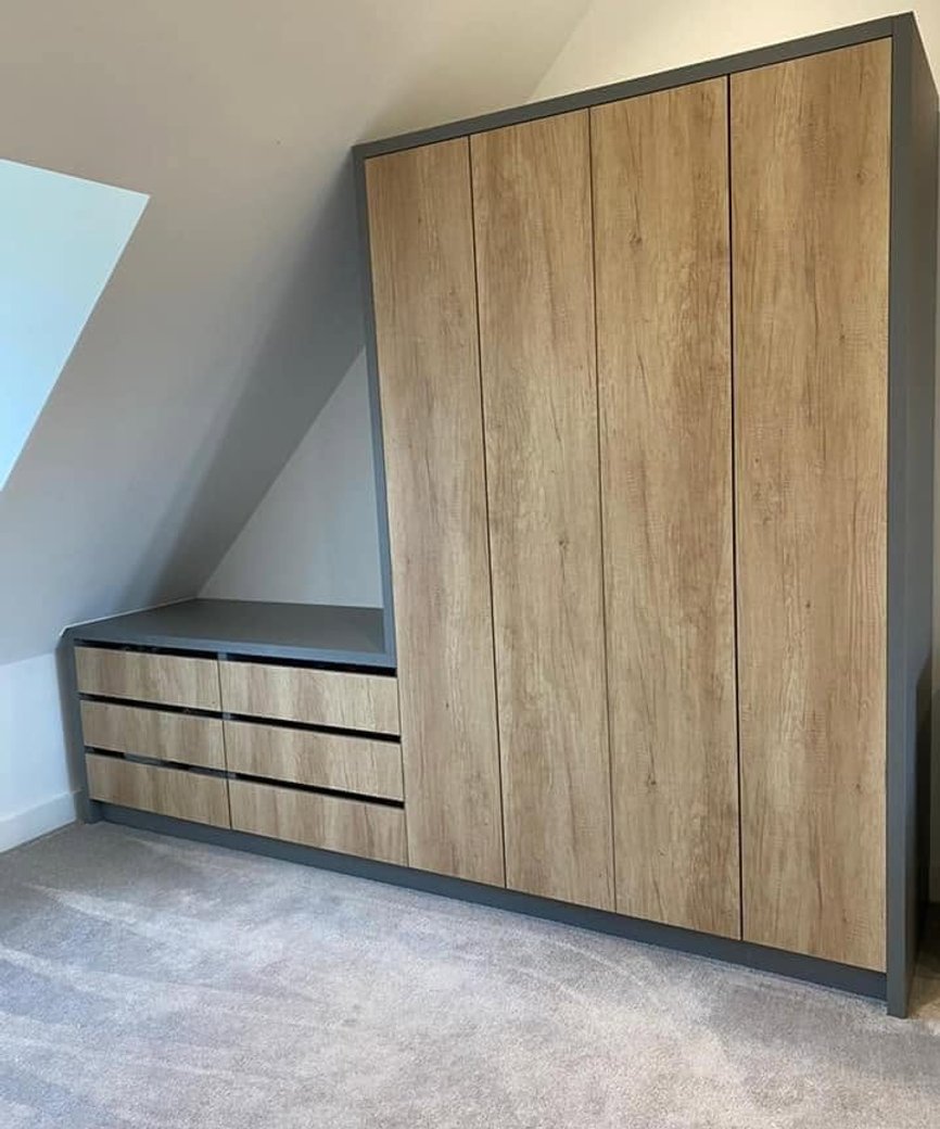 Wood-effect fitted wardrobe and drawers beneath a sloping bedroom ceiling