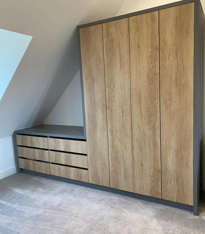Wood-effect fitted wardrobe with matching drawers beneath a sloping ceiling