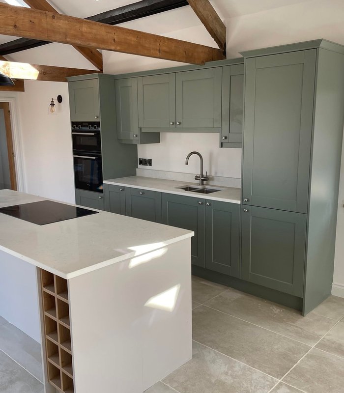 Green shaker kitchen with an island, stone wall and exposed beams