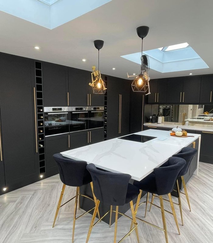 Dark fitted kitchen with an island, brass handles and rooflights